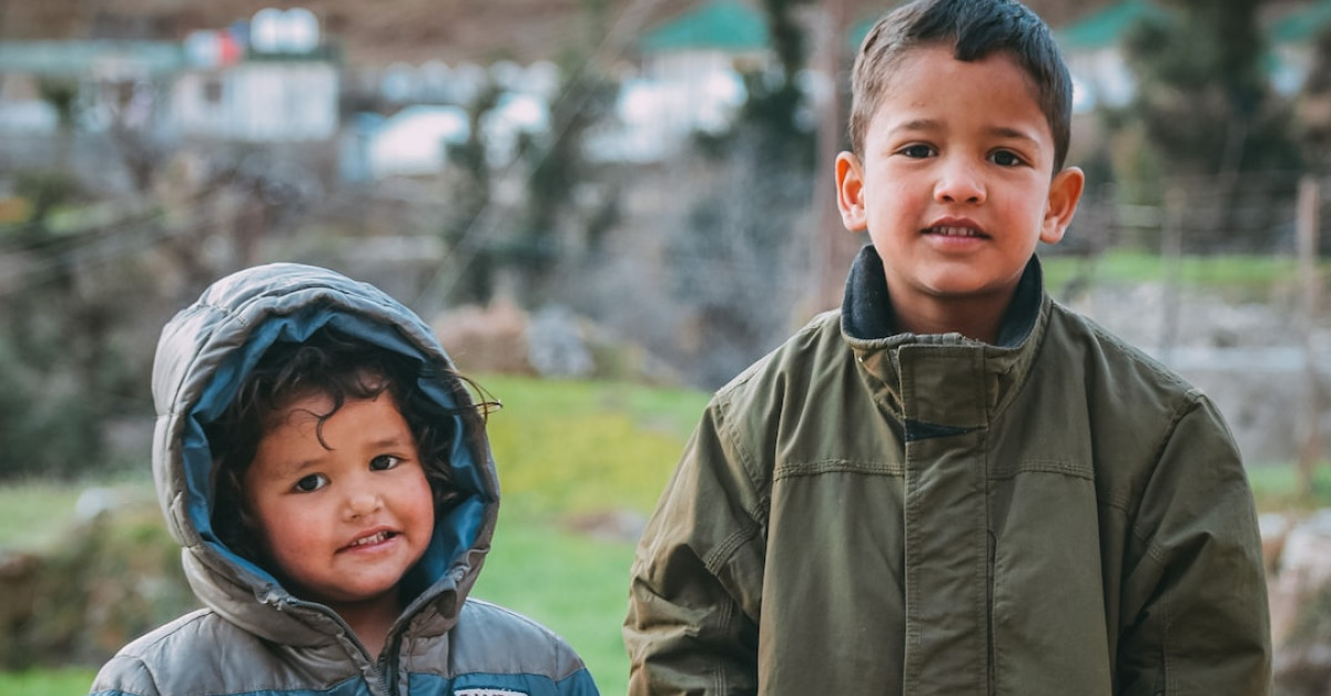 Kids riding electric scooters outdoors with safety gear on.